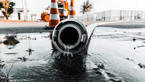 Discharge hose pumping water out onto wet pavement