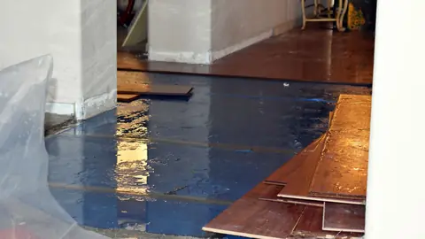 Hardwood boards pulled up over a wet blue underlayment during floor water damage repair